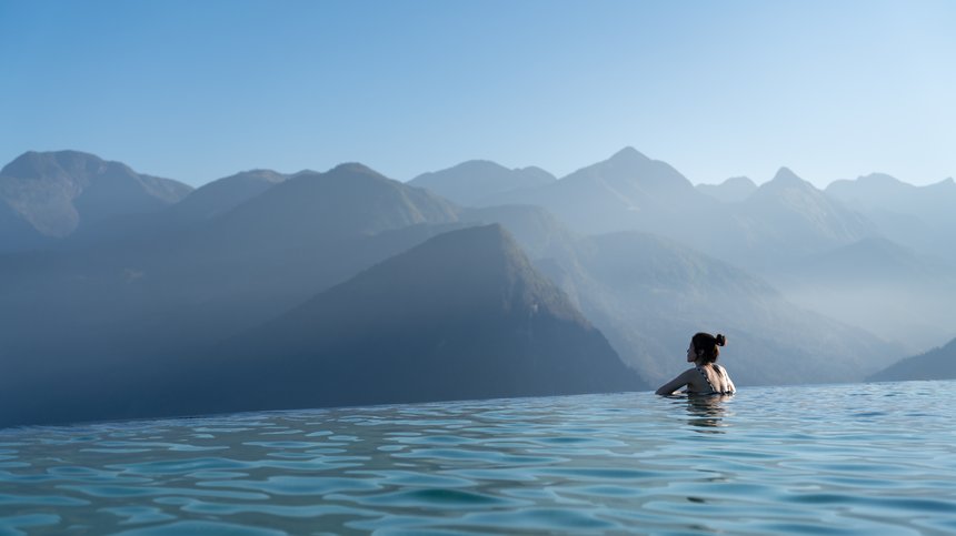 Geheimtipp Hotels in Südtirol 😎☀️ Frau in Infinity-Pool mit Blick auf nebelige Berglandschaft bei klarem Himmel