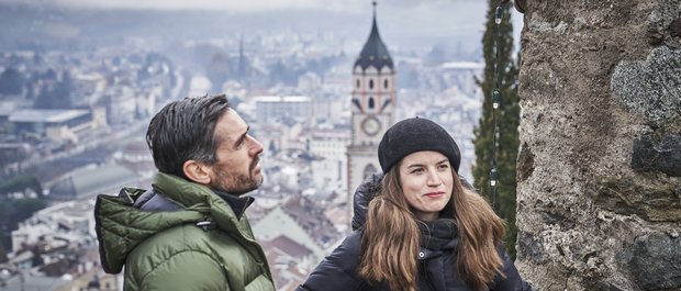 Geheimtipp Hotels in Südtirol 😎☀️ Paar in Winterkleidung vor einer Stadtansicht mit Kirchturm im Hintergrund
