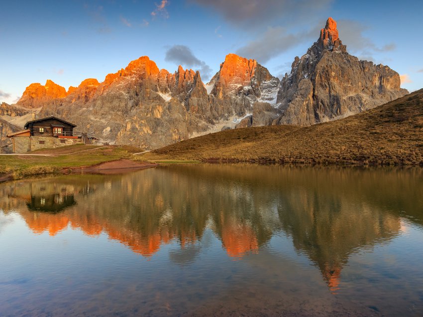 Geheimtipp Hotels in Südtirol 😎☀️ Almhütte mit Bergspitzen im warmen Abendlicht und Spiegelung im See