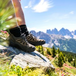 Die schönsten Motorradstrecken in Südtirol Wanderschuhe auf Felsen mit Bergpanorama und grüner Landschaft im Hintergrund