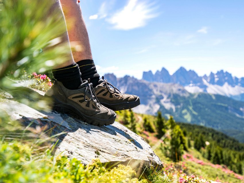Geheimtipp Hotels in Südtirol 😎☀️ Wanderschuhe auf Felsen mit Bergpanorama und grüner Landschaft im Hintergrund