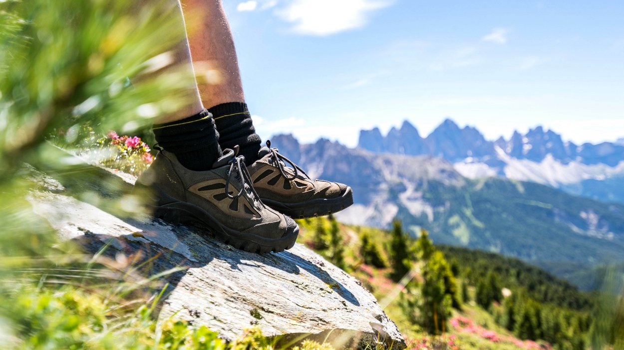 Escursioni in Alto Adige: esperienze indimenticabili! Scarpe da trekking su roccia con panorama di montagne e paesaggio verde sullo sfondo