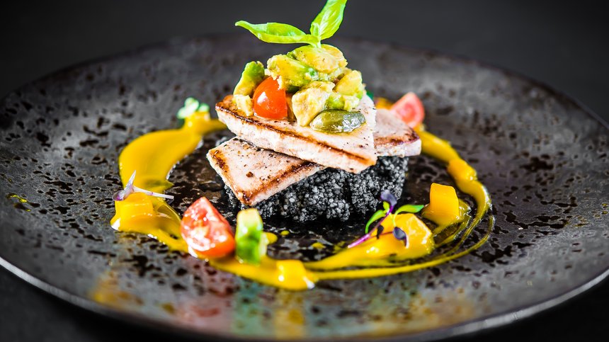 Geheimtipp Hotels in Südtirol 😎☀️ Gourmetgericht mit gegrilltem Fisch, Avocado und Gemüse auf schwarzem Teller