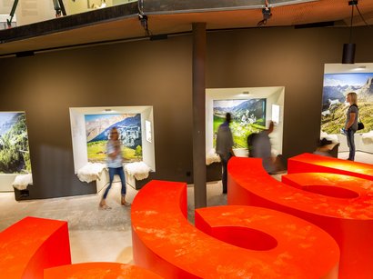 L‘Epifania Interno con sedute rosse e persone davanti a fotografie di montagne