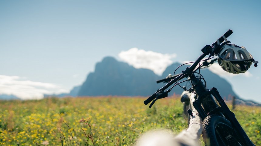 Geheimtipp Hotels in Südtirol 😎☀️ Mountainbike lehnt an Holzzaun vor blumiger Wiese mit Berg im Hintergrund
