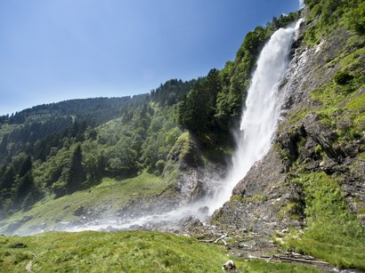 L‘Epifania Cascata che scende da una montagna rocciosa in un paesaggio verde