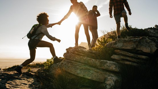 Lampskopf-Klettersteig zur Tribulaunhütte Gruppe von Freunden beim Wandern helfen sich gegenseitig auf Felsen bei Sonnenuntergang