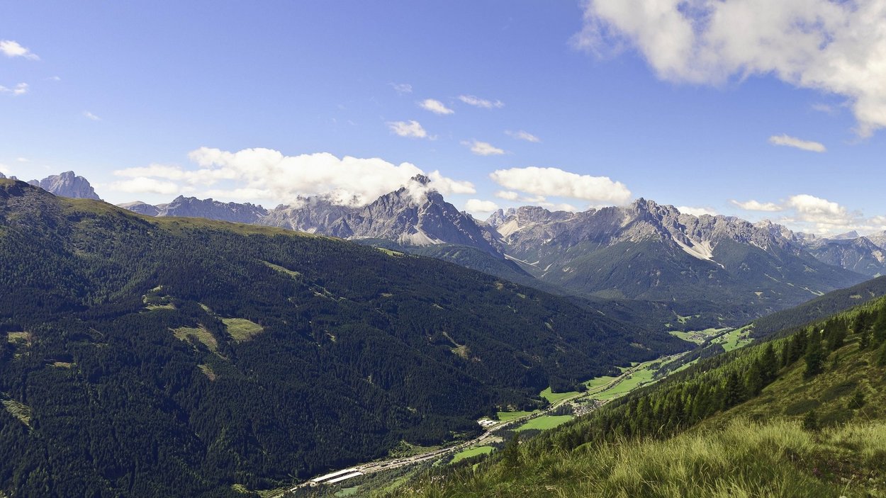 Die schönsten Motorradstrecken in Südtirol Panoramablick auf bewaldete Berge und ein Tal unter blauem Himmel