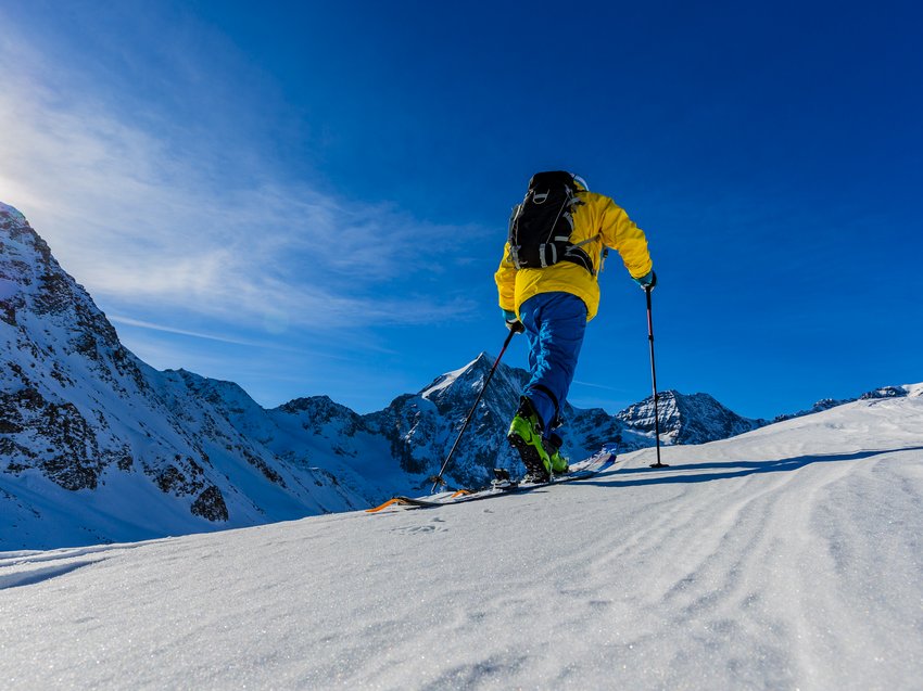 Geheimtipp Hotels in Südtirol 😎☀️ Skifahrer in gelber Jacke fährt auf schneebedecktem Berg bei sonnigem Himmel