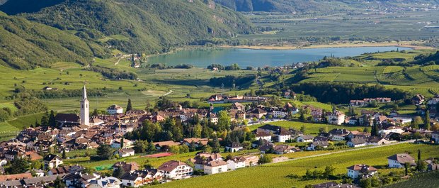 Geheimtipp Hotels in Südtirol 😎☀️ Blick auf ein Dorf mit Kirche, umgeben von Weinbergen und einem See in den Bergen
