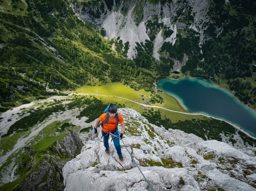 Geheimtipp Hotels in Südtirol 😎☀️ Kletterer in orange am Berg mit Blick auf See und grüne Landschaft