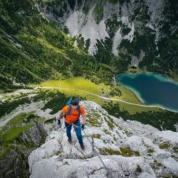 Escursioni in Alto Adige: esperienze indimenticabili! Alpinista con maglia arancione arrampicata su roccia con vista su lago e natura verde