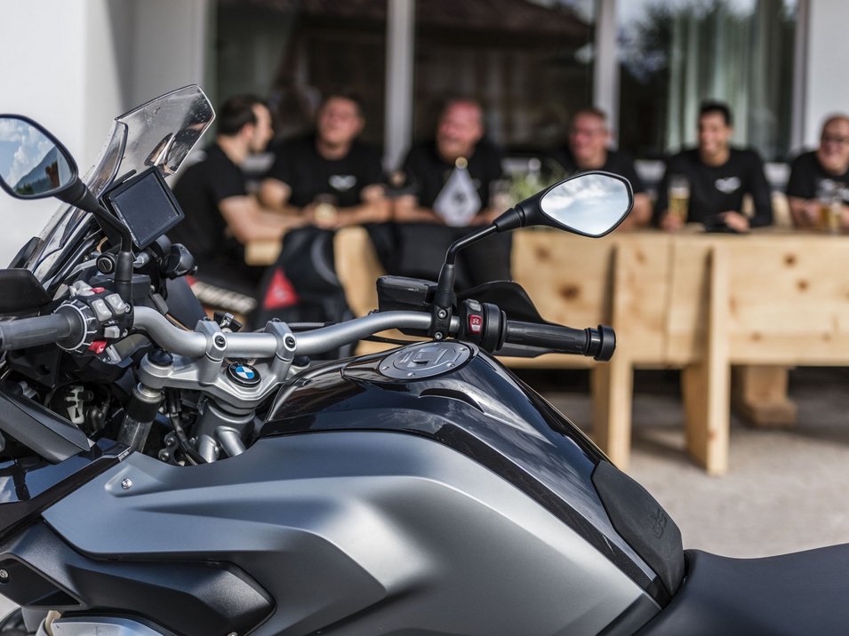 Die schönsten Motorradstrecken in Südtirol Motorrad im Vordergrund, Menschen sitzen im Hintergrund an einem Holztisch