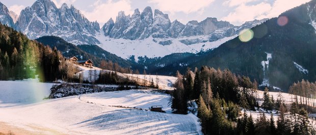 Geheimtipp Hotels in Südtirol 😎☀️ Schneebedeckte Almwiese vor markanten Dolomiten mit Häusern im Sonnenlicht