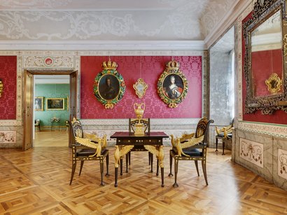 L‘Epifania Stanza elegante con pareti rosse, sedie dorate e ritratti alle pareti