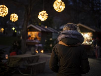 Die Entstehung eines altbekannten Brauches Person in Winterjacke bei beleuchtetem Weihnachtsmarkt am Abend
