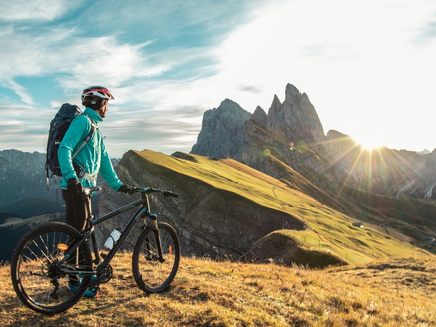Geheimtipp Hotels in Südtirol 😎☀️ Radfahrer mit Helm schaut auf Bergpanorama bei Sonnenuntergang