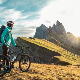 Escursioni in Alto Adige: esperienze indimenticabili! Ciclista con casco osserva un panorama montano al tramonto