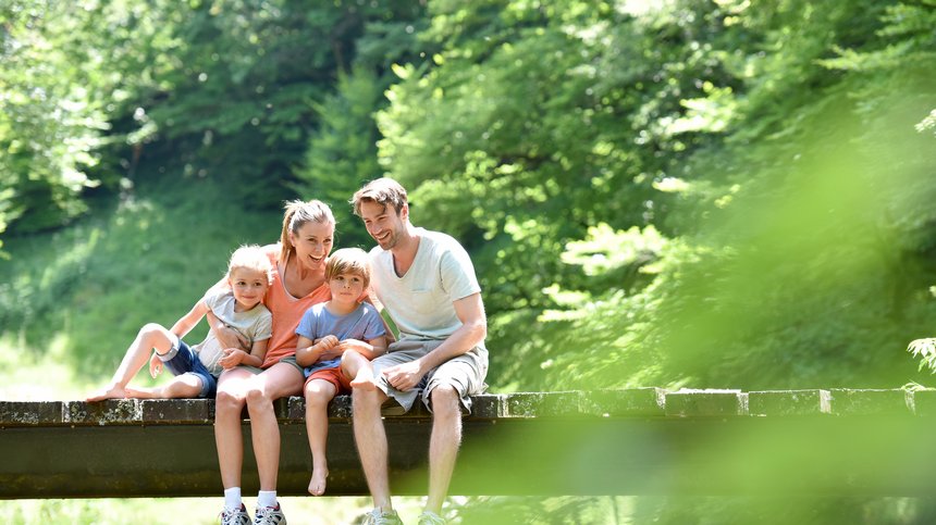 Geheimtipp Hotels in Südtirol 😎☀️ Glückliche Familie mit zwei Kindern sitzt auf einer Brücke in der Natur