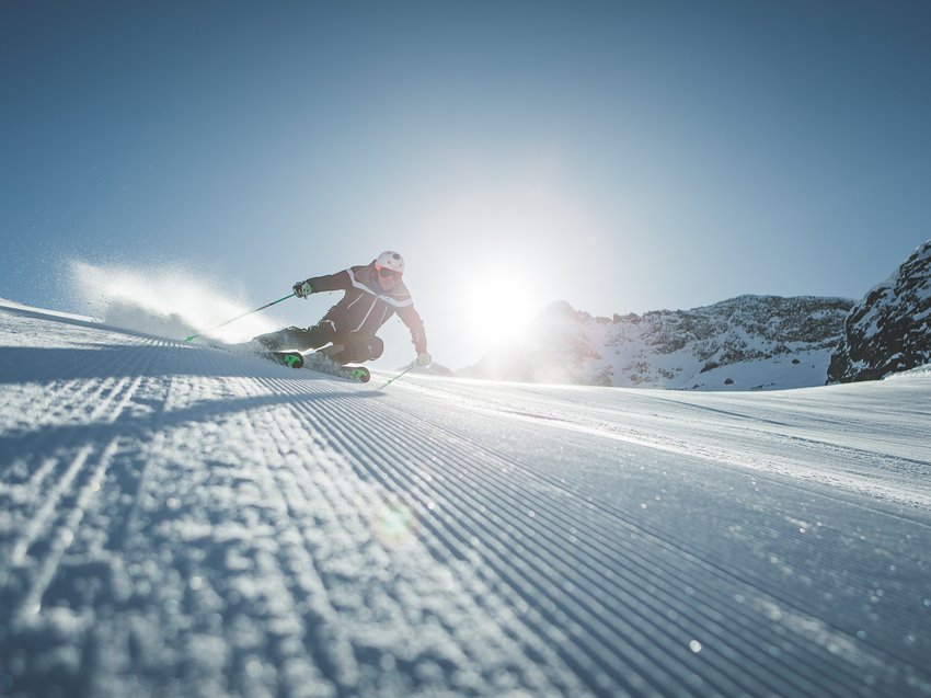 Geheimtipp Hotels in Südtirol 😎☀️ Skifahrer bei Abfahrt auf präparierter Piste mit Sonne und Bergen im Hintergrund