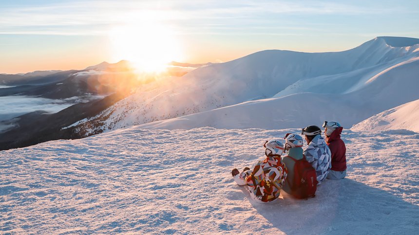 Geheimtipp Hotels in Südtirol 😎☀️ Vier Personen in Skiausrüstung sitzen im Schnee und schauen auf den Sonnenuntergang
