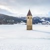 Transumanza in Alto Adige: un’importante tradizione Campanile che emerge da lago ghiacciato in paesaggio montano innevato